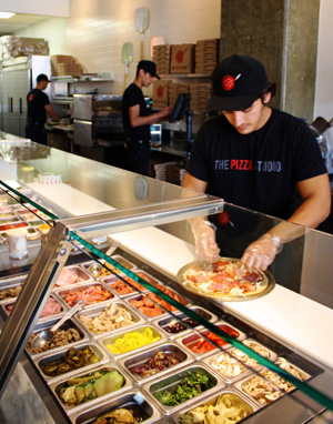 Employee in Pizza Studio builds a customer’s pizza based on the customer’s choice of topping.

