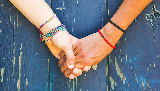 Two women holding hands with a wooden background. One is caucasian, the other is black. Multicultural, homosexual love and friendship concepts.